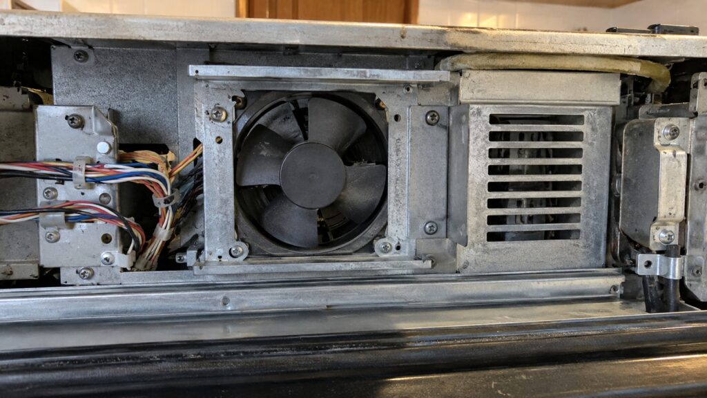 The cooling fan and ventilation slot in the electronics bay behind the control panel of a wall oven, with the panel removed