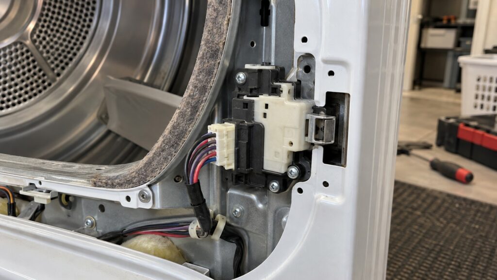 A close view of the door lock actuator and its wiring harness in the front panel of a dryer with the panel removed