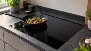 A black induction cooktop set into a dark countertop with a single pan on one cooking zone
