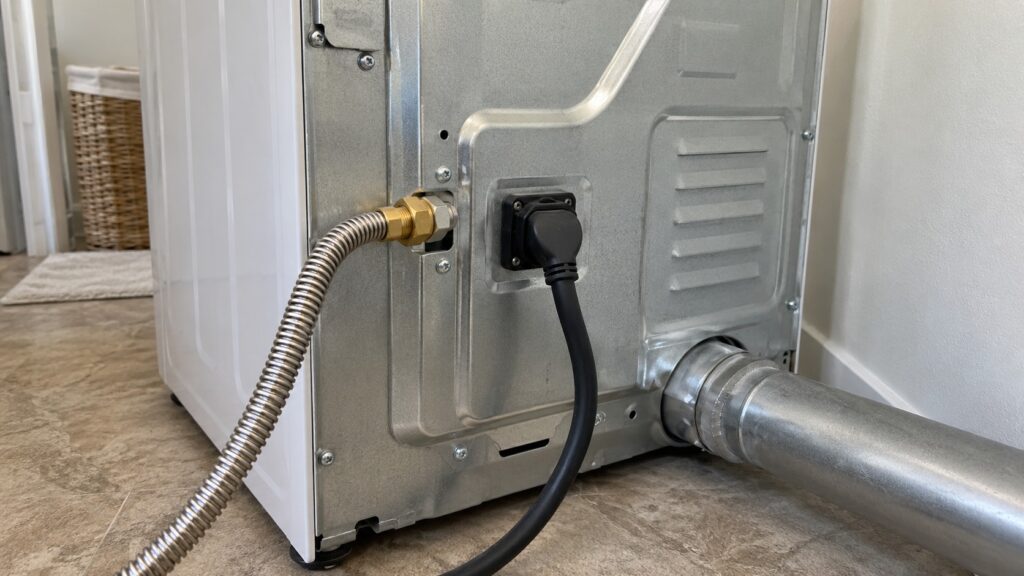 The rear of a freestanding dryer showing a flexible gas line fitting beside the power cord connection