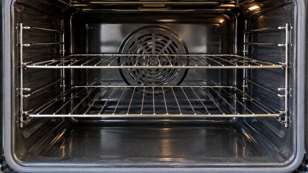 The inside of an empty oven cavity showing the fan cover at the back wall and two wire racks