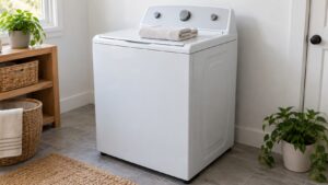 A top-load washer standing in a clean laundry room against a white wall with a folded towel on its lid
